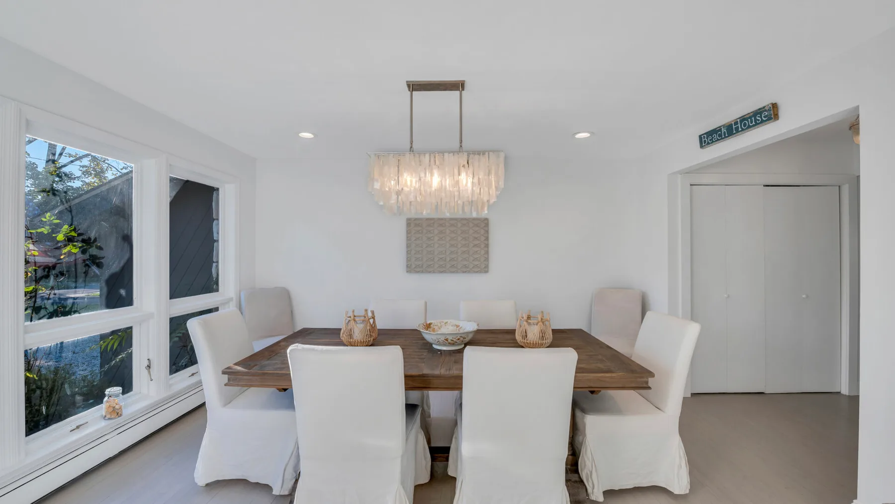 Un comedor luminoso con una mesa de madera, asientos tapizados y una lámpara de araña.