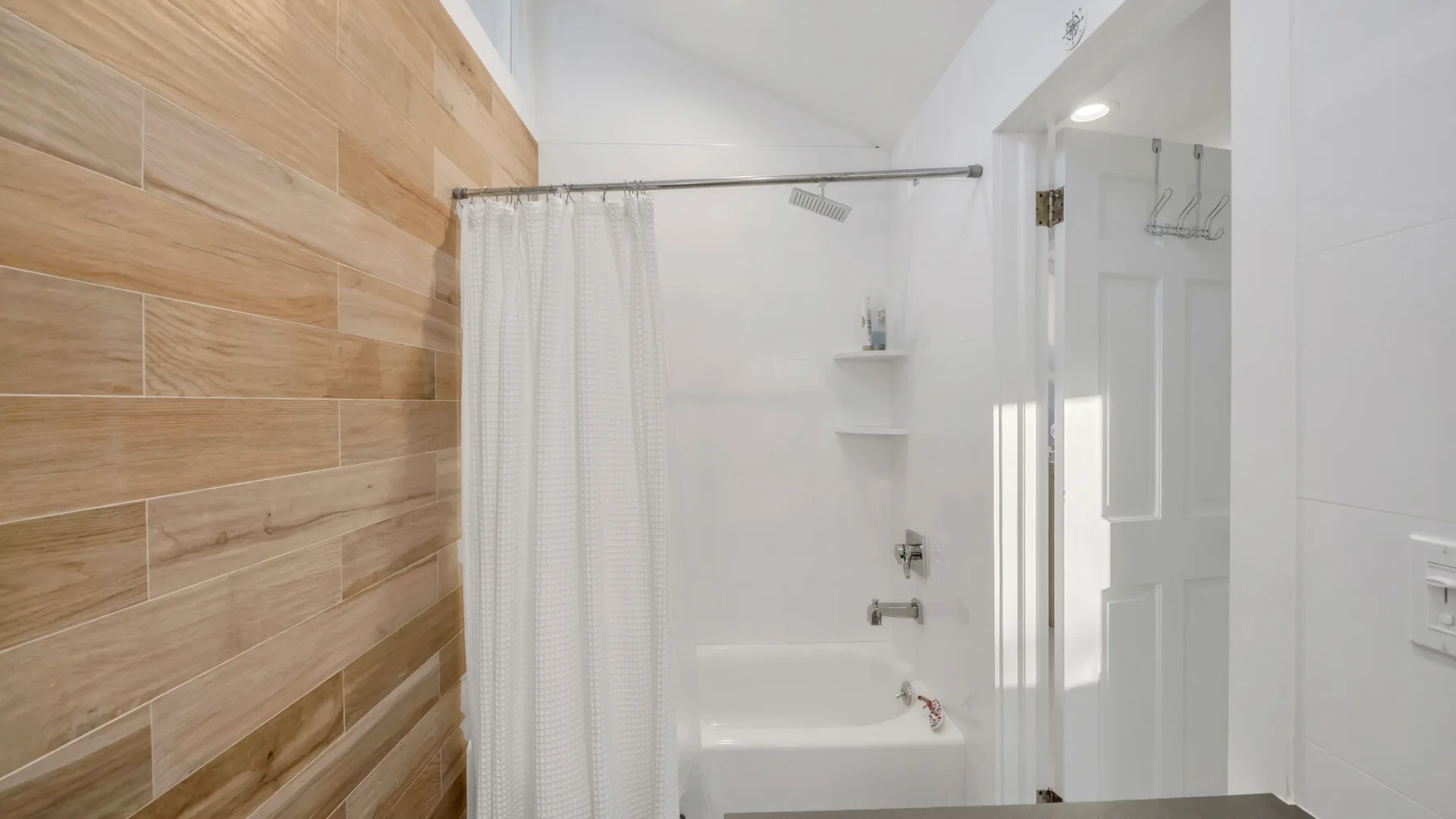 Un baño con bañera y cortina de ducha junto a una pared de azulejos efecto madera.
