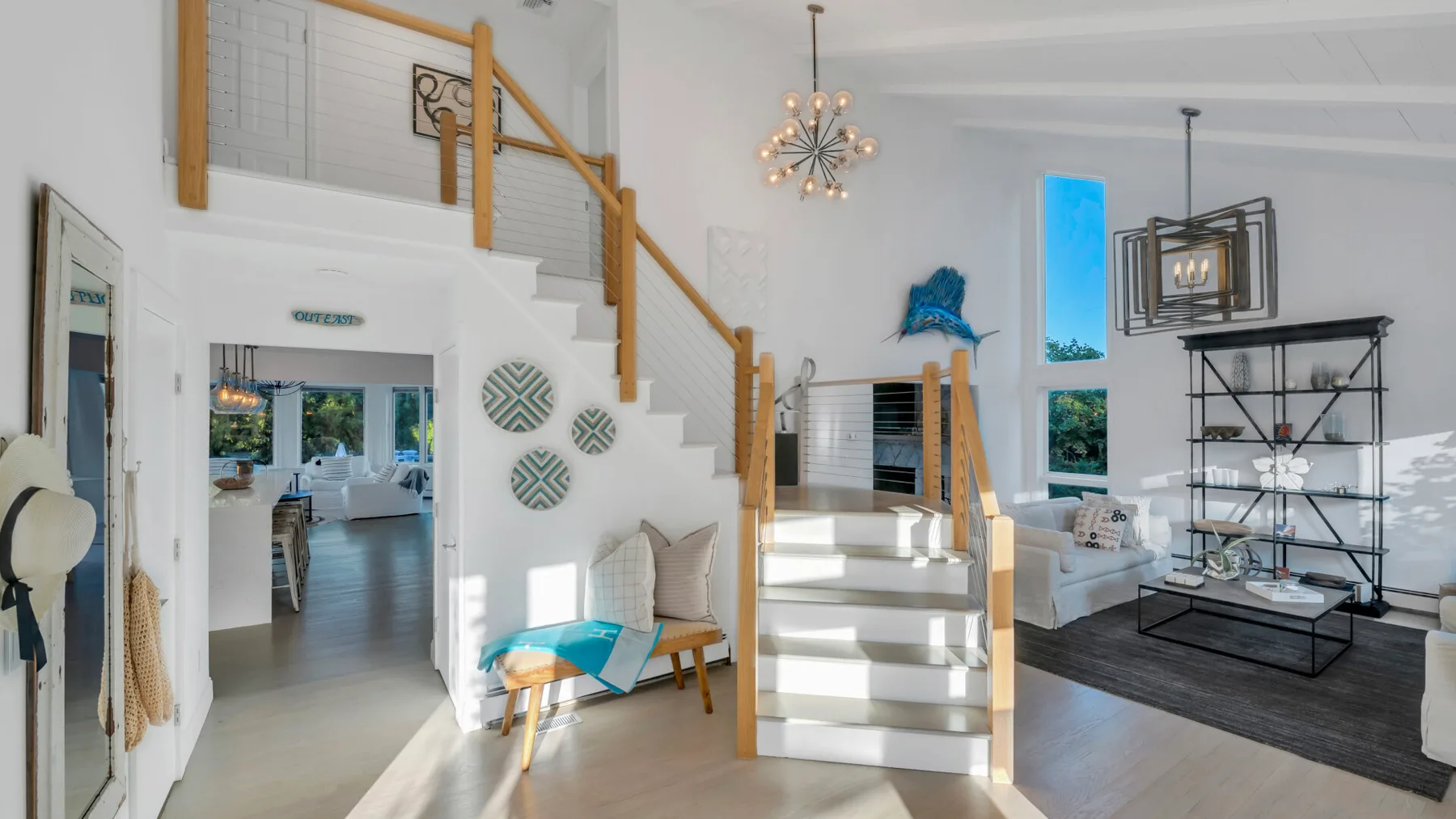 Una luminosa sala de estar abierta con una escalera, asientos y ventanas grandes.