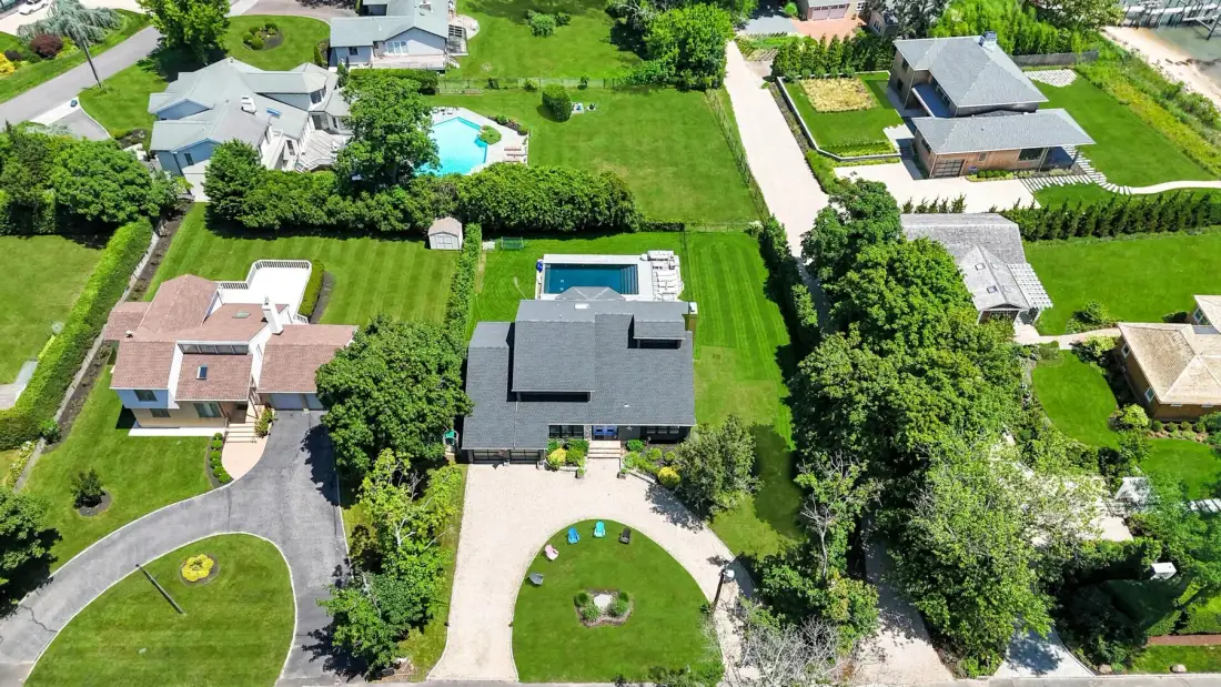 Una vista aérea muestra varias casas, céspedes verdes y una piscina.