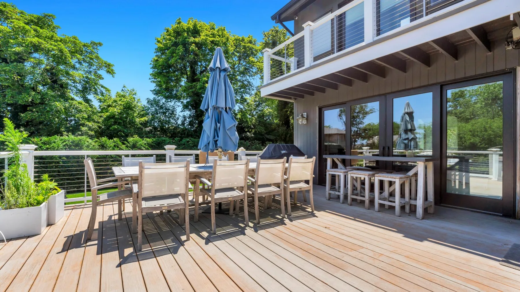 Una terraza exterior junto a una casa, con mesa, asientos y una sombrilla cerrada.