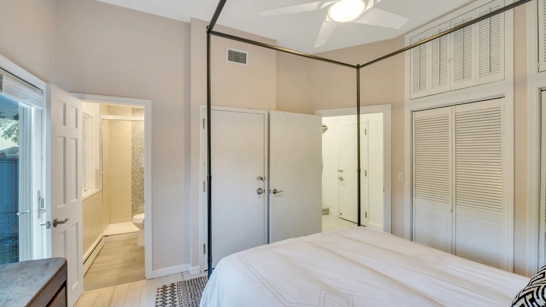 Dormitorio con una cama, puertas de armario con persianas y una entrada abierta al baño.