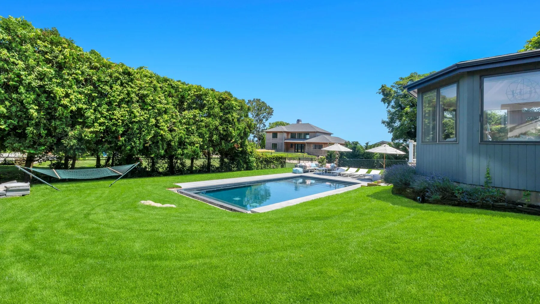 Un patio ajardinado con piscina, césped, árboles y un edificio.