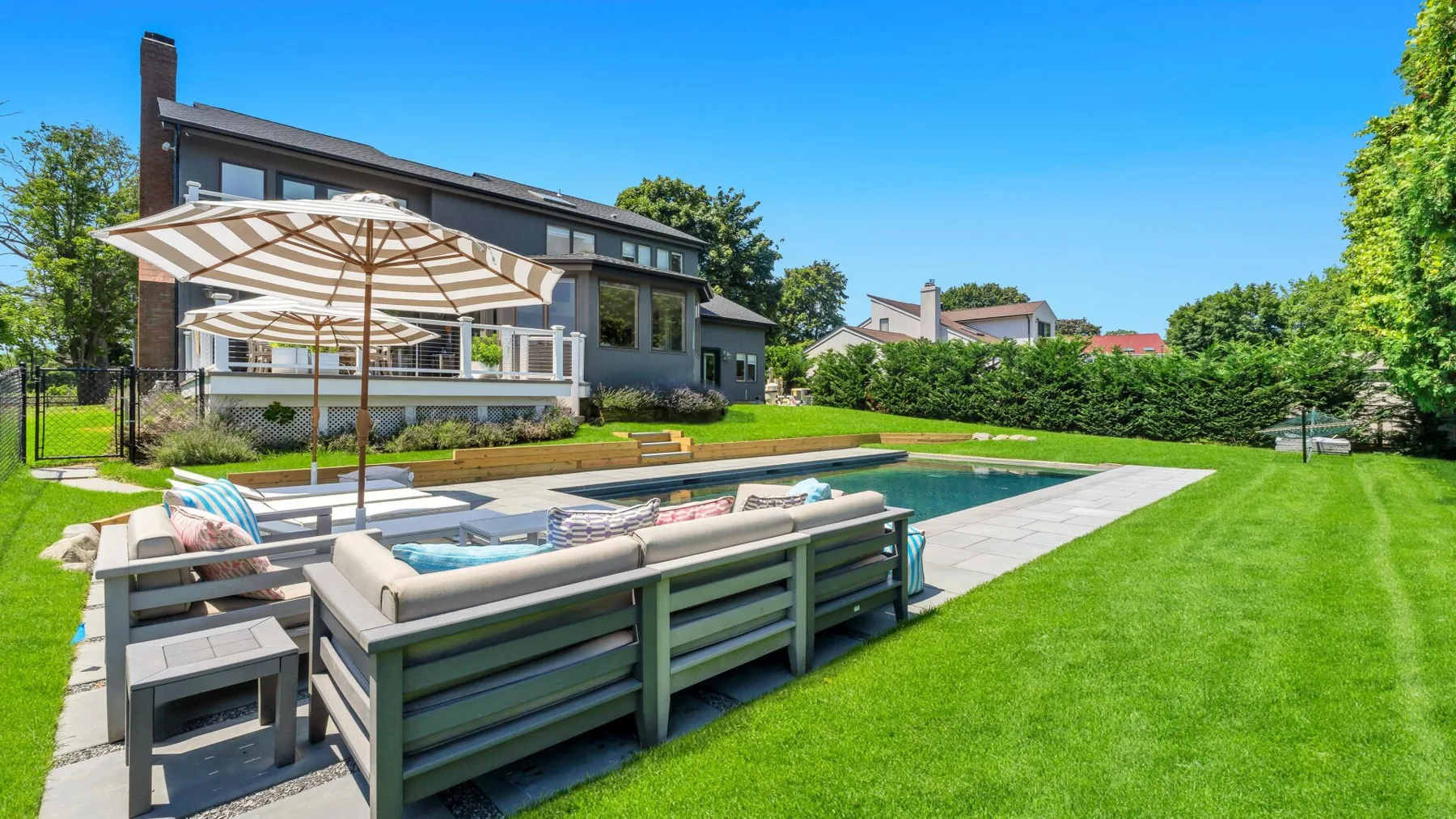 A landscaped backyard with a swimming pool, outdoor seating, and a large house.