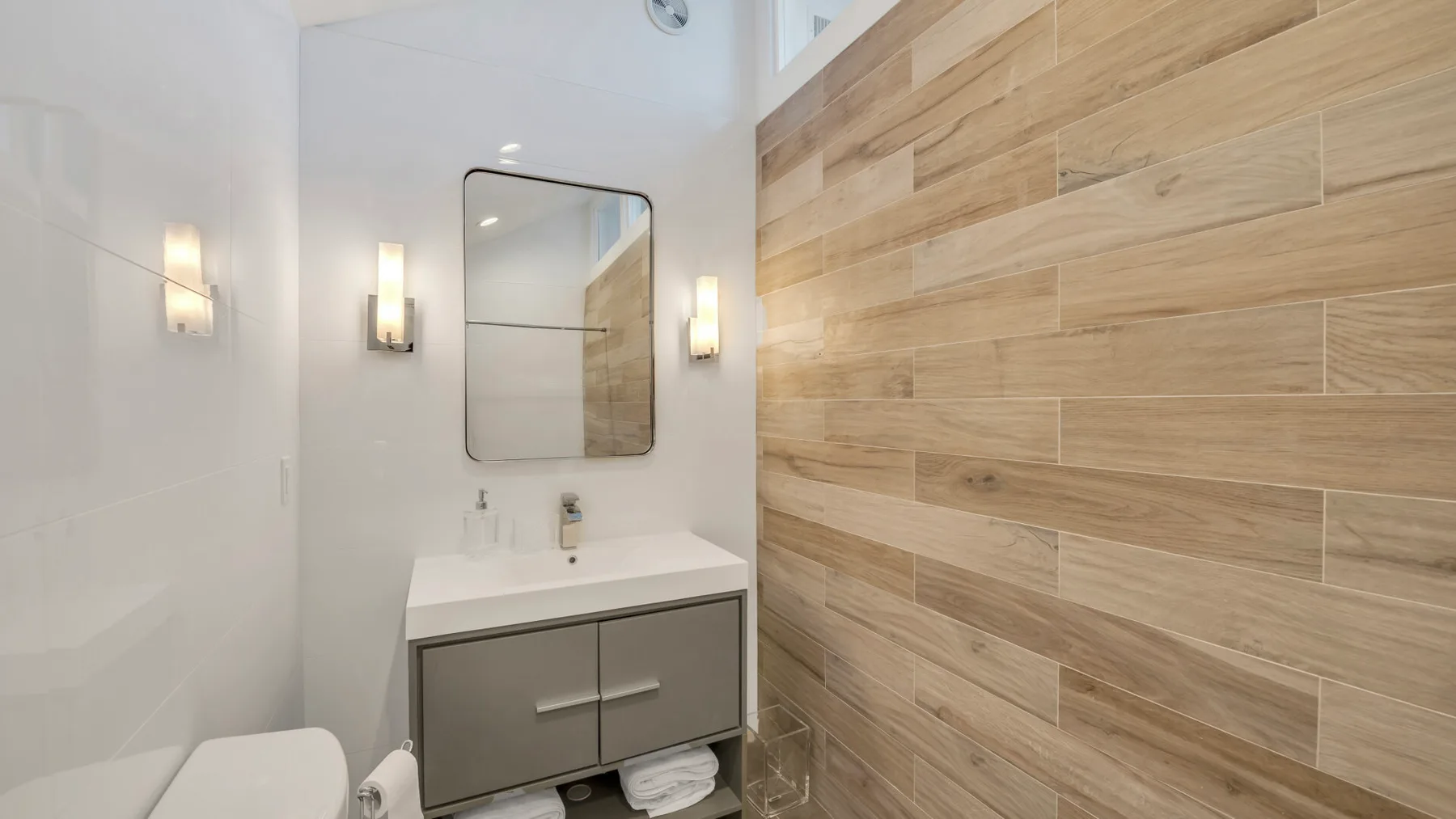 Un baño con lavabo, espejo y azulejos de pared con aspecto de madera.