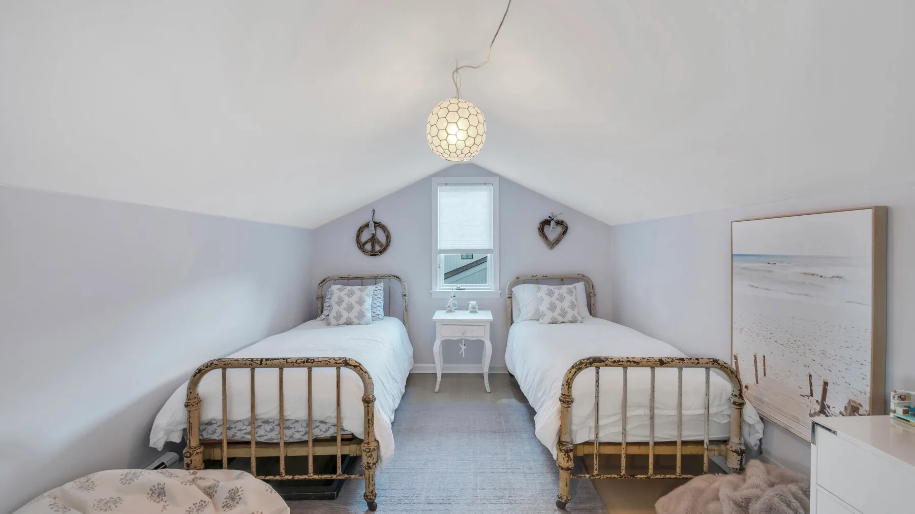 Un dormitorio abuhardillado luminoso con camas individuales y una mesita entre ellas.