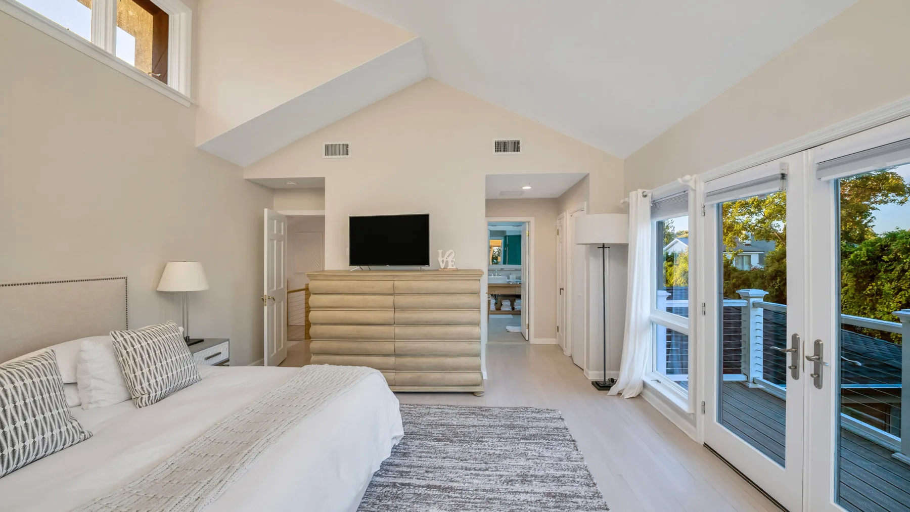 Un dormitorio luminoso con una cama, un televisor y puertas de vidrio que dan a un balcón.