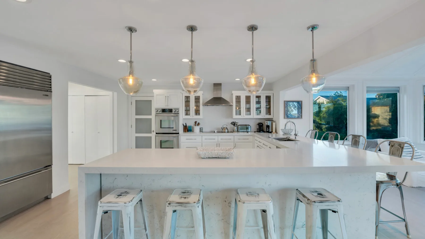 Una cocina luminosa con una isla grande, lámparas colgantes y ventanas.