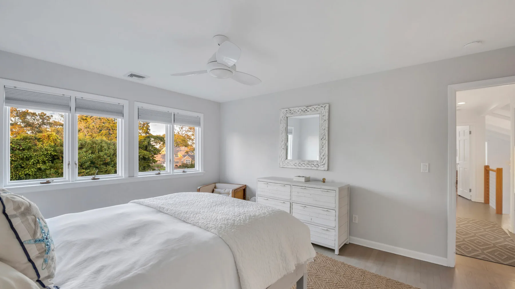 Un dormitorio luminoso con una cama, ventanas y una cómoda blanca.