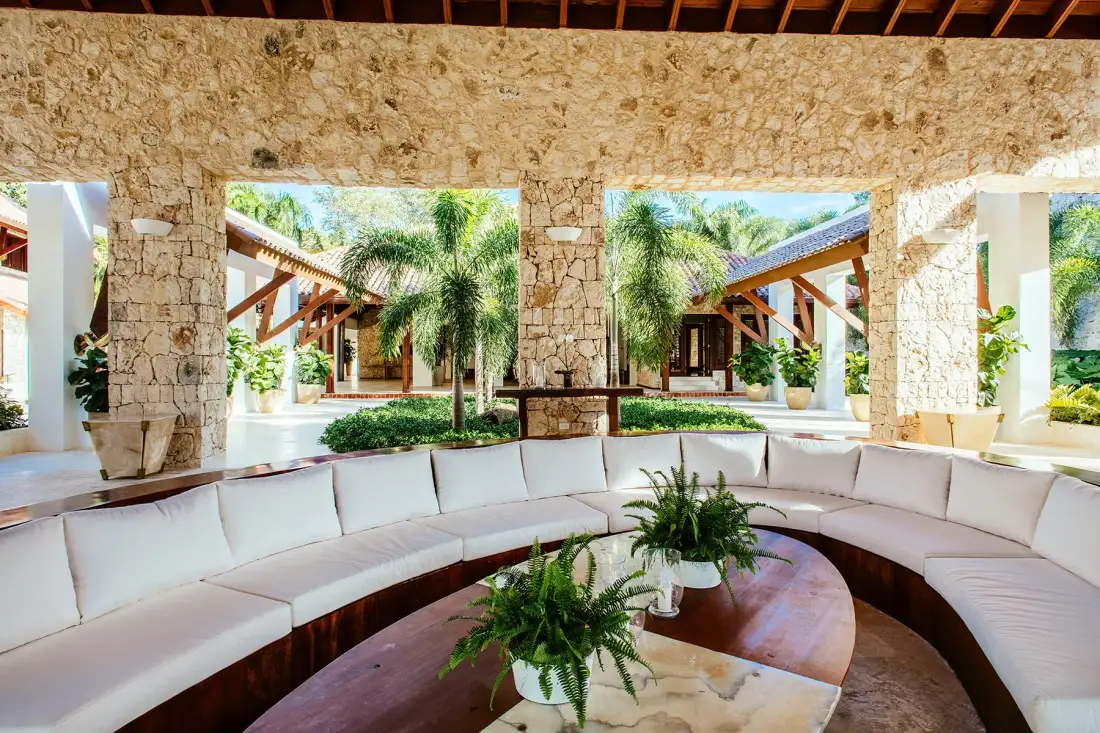 An open-air lounge with curved seating and plants beneath a stone wall.