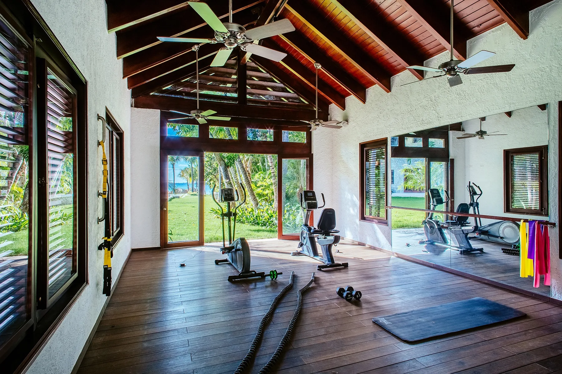 A bright home gym with exercise equipment, large windows, and a vaulted timber ceiling.