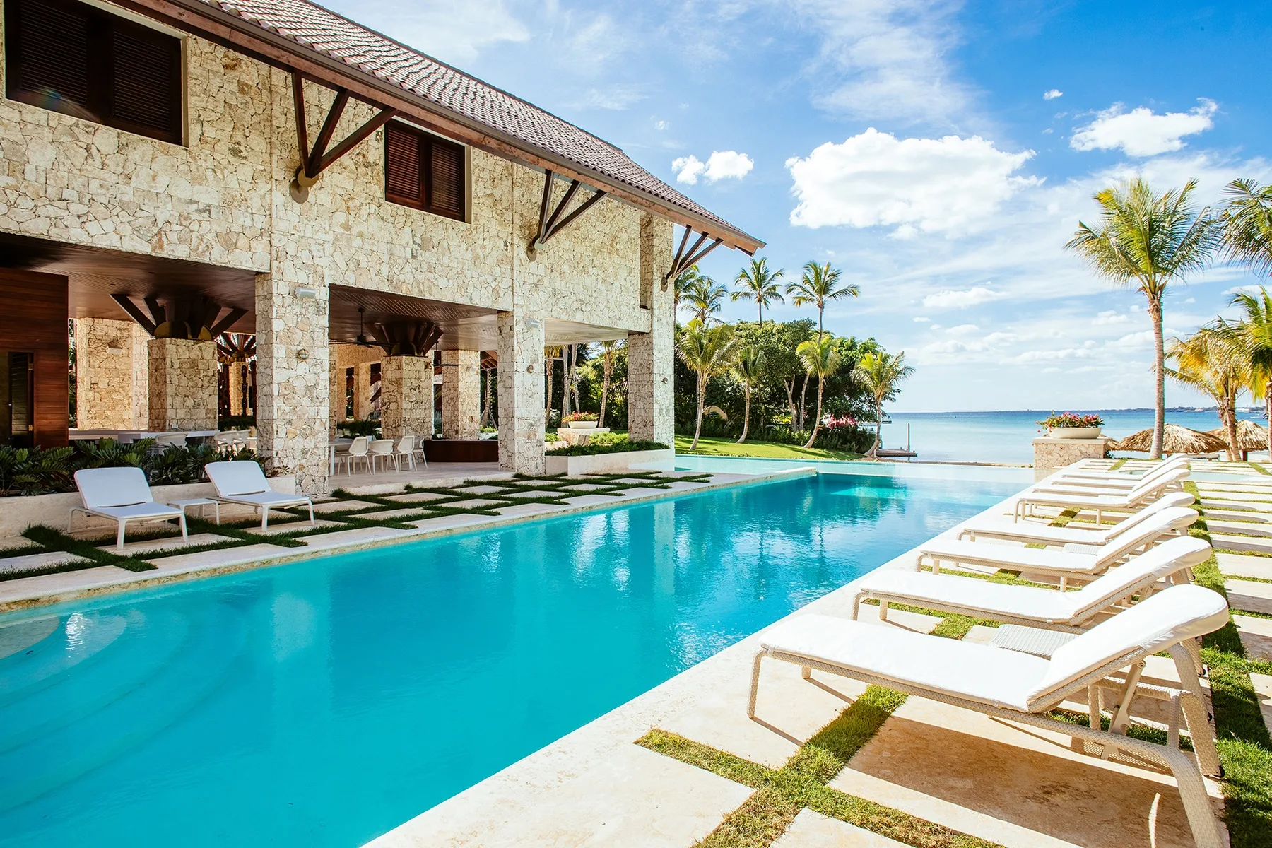 A swimming pool beside a stone building, with lounge chairs and the ocean beyond.