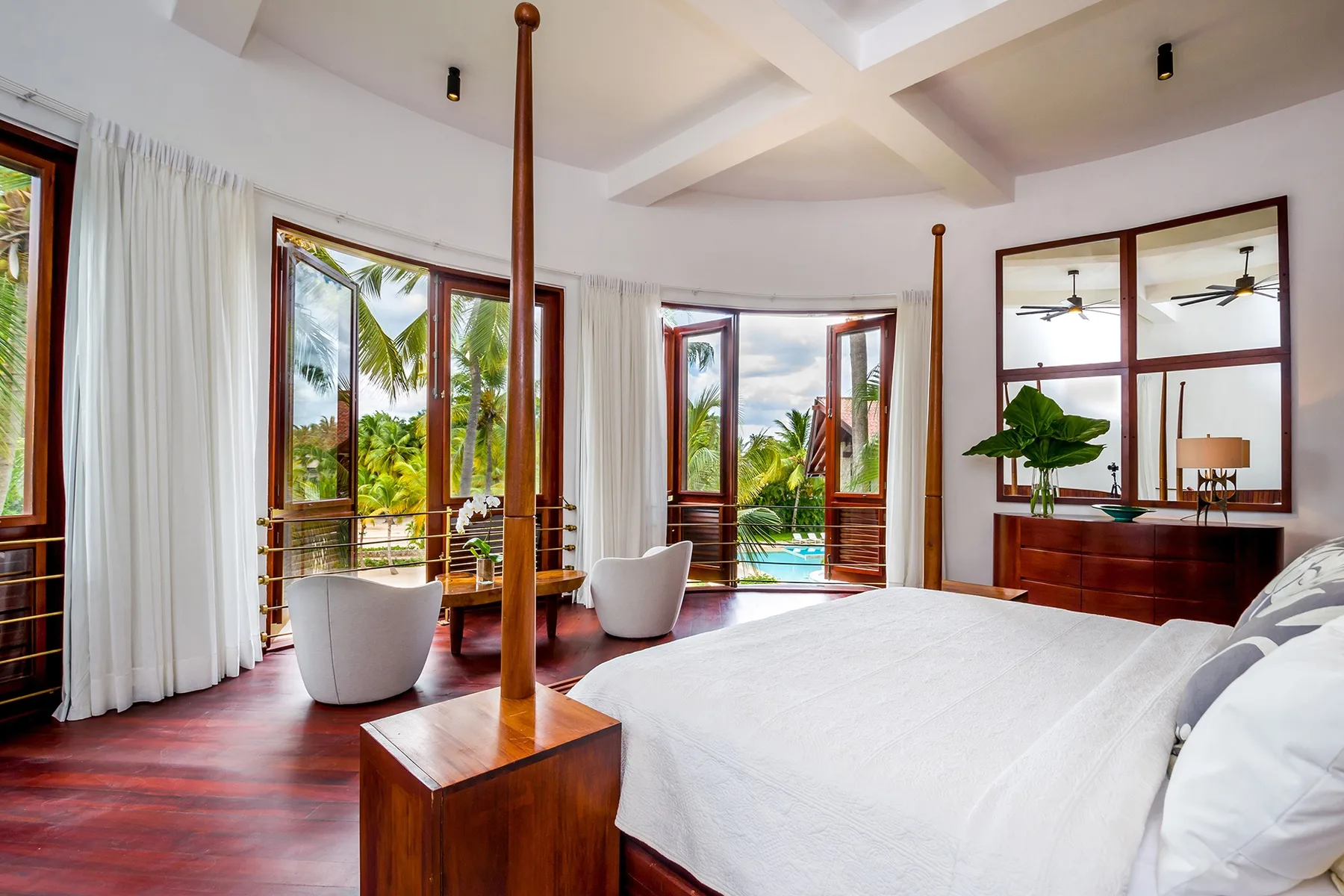A bright bedroom opens onto tropical greenery through large glass doors.