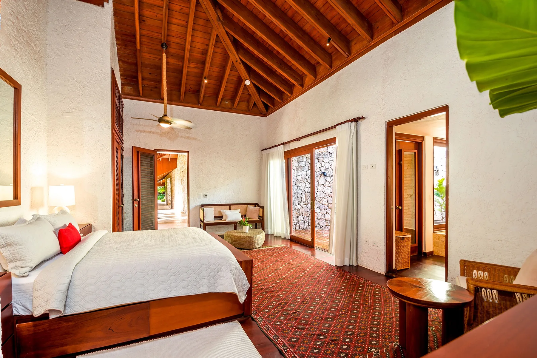 A bedroom with a large bed, patterned rug, and exposed wooden ceiling.