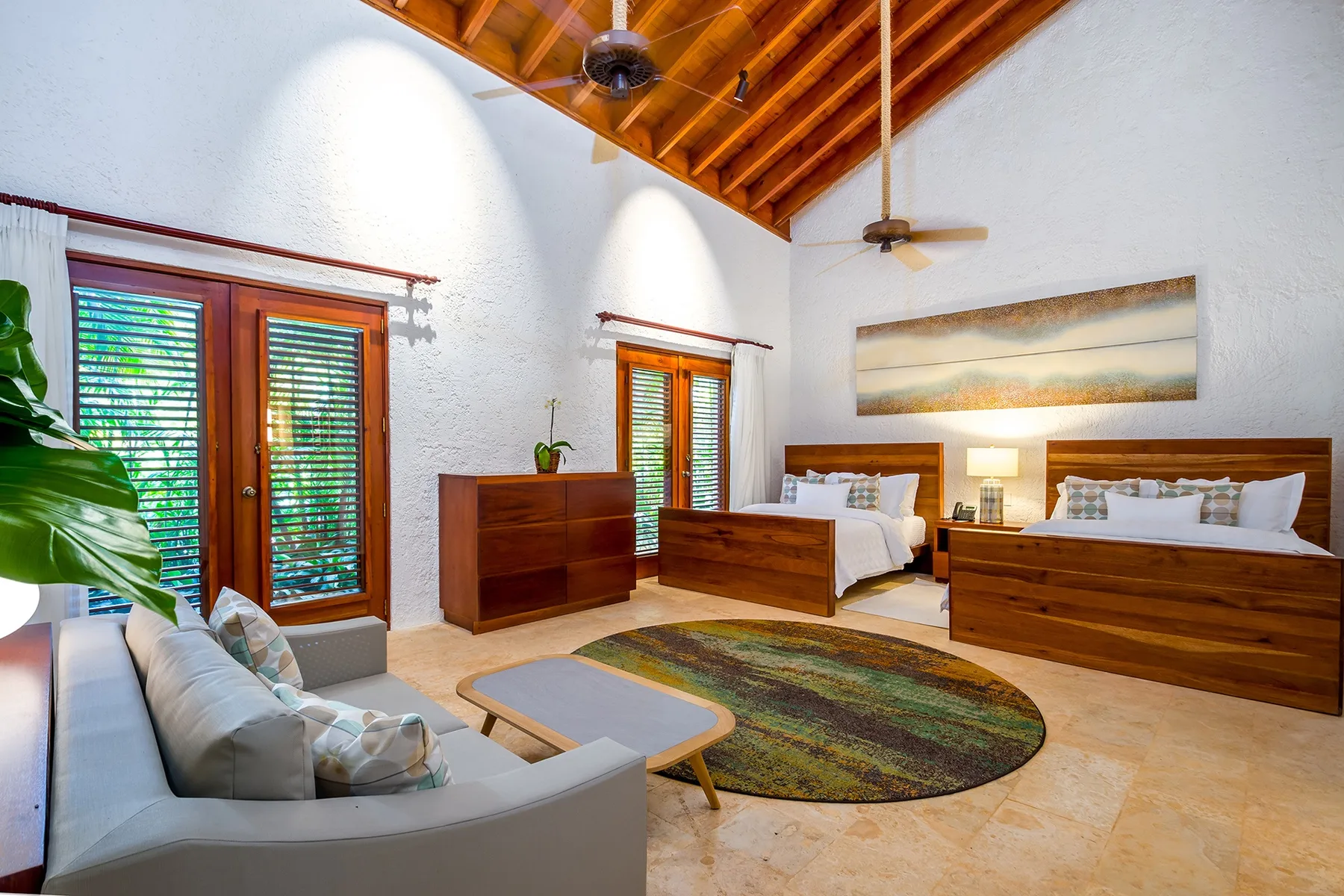 A bedroom with two beds, a seating area, and a wooden vaulted ceiling.