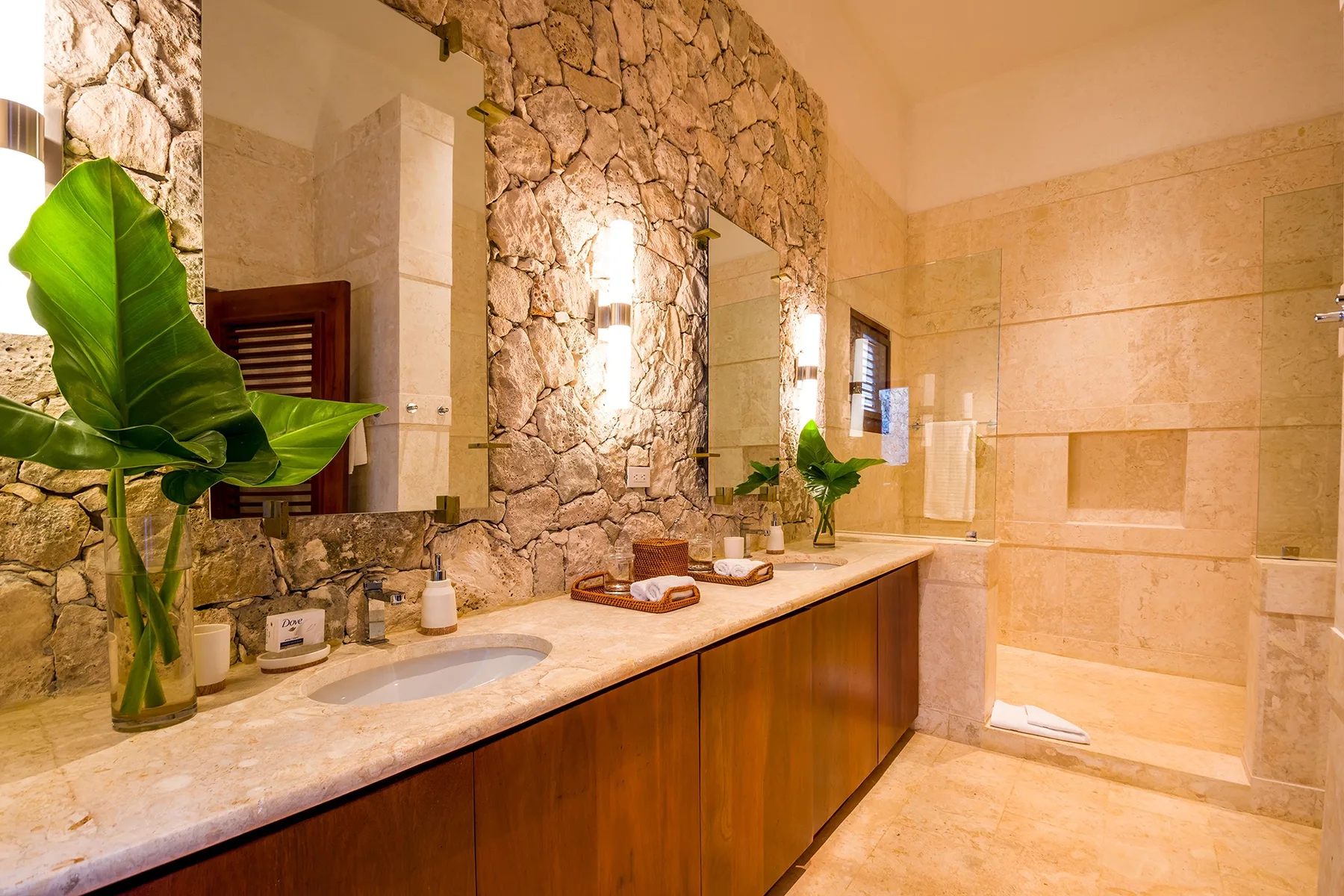 A stone-walled bathroom with a long vanity and a walk-in shower.