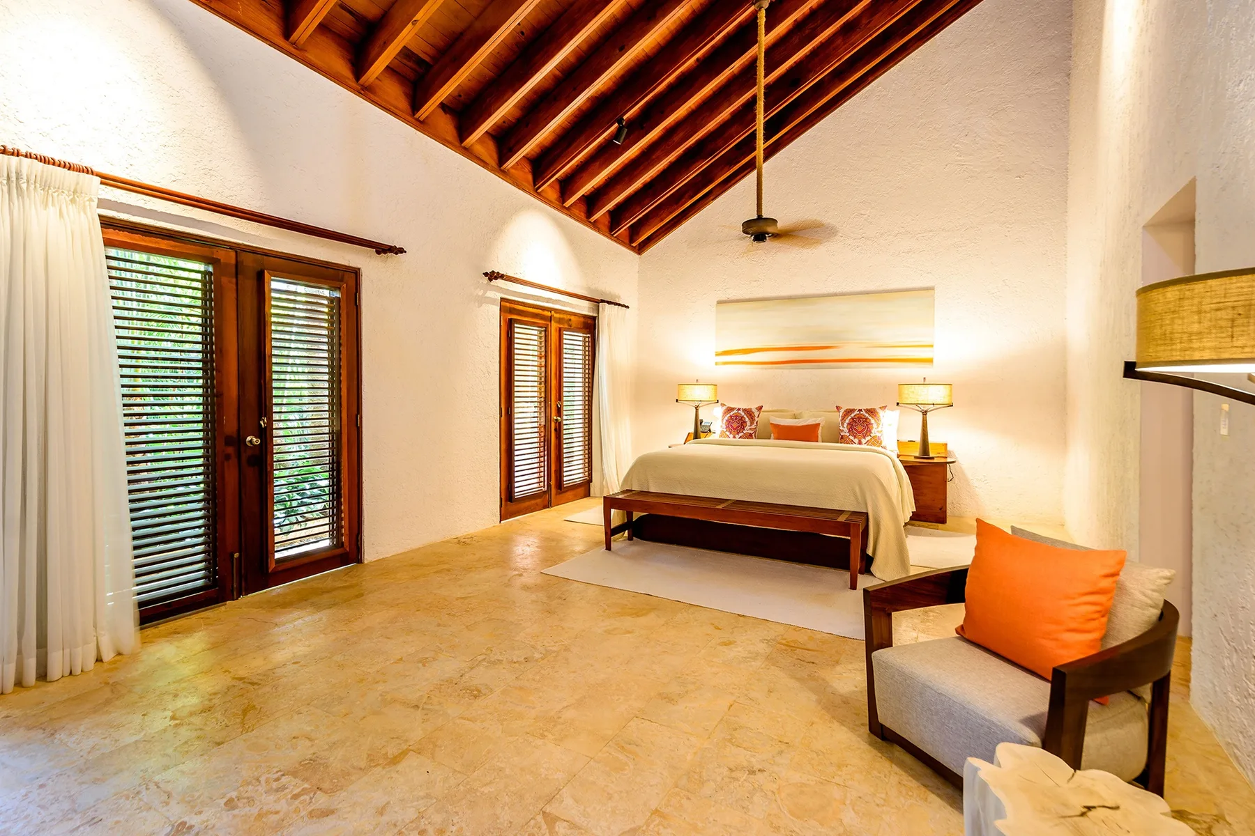 A bright bedroom with a bed, wood-beamed ceiling, and an armchair.