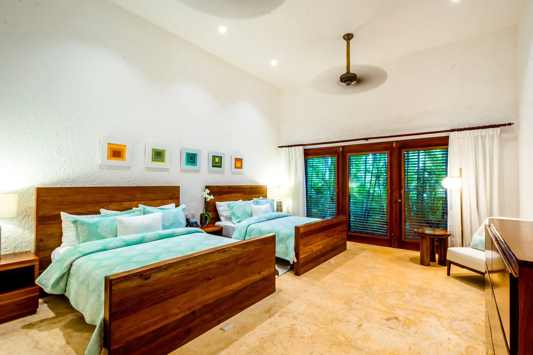 A bright bedroom with two wooden beds and large windows with blinds.
