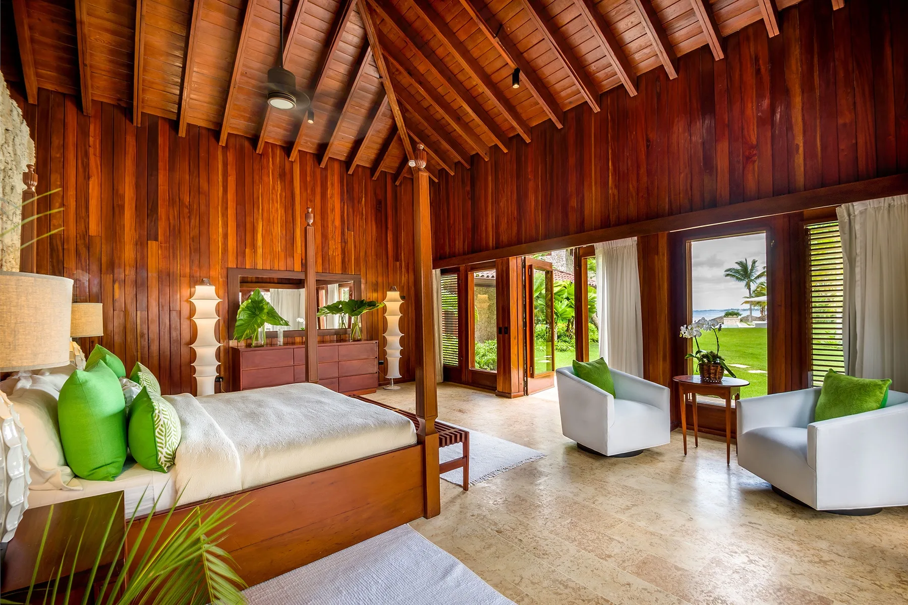 A bedroom with a wooden bed and a sitting area beside wide windows.