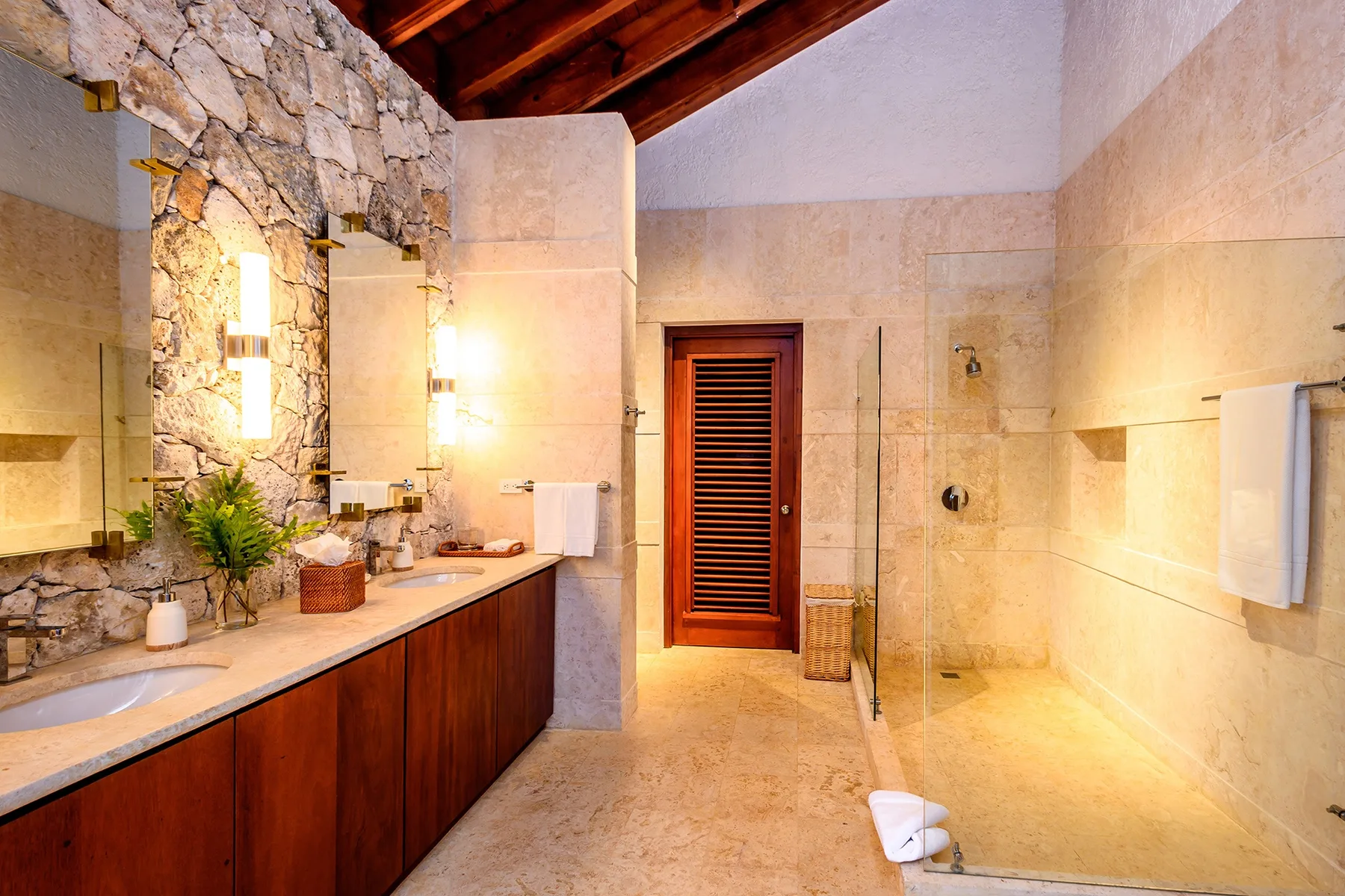 A stone bathroom with a long vanity, mirror, and glass shower.