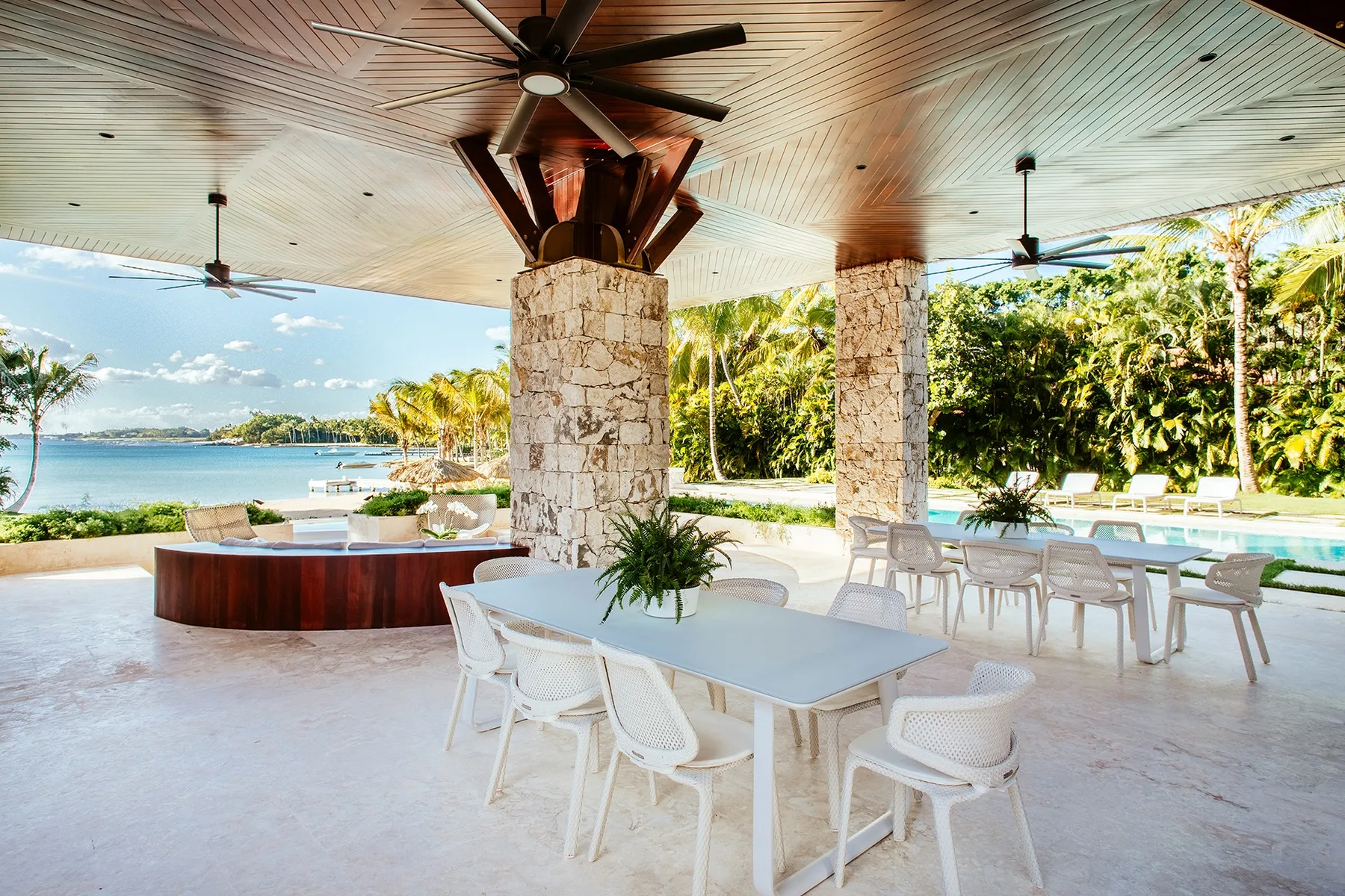 An open-air dining area with tables and seating overlooks a tropical waterfront.