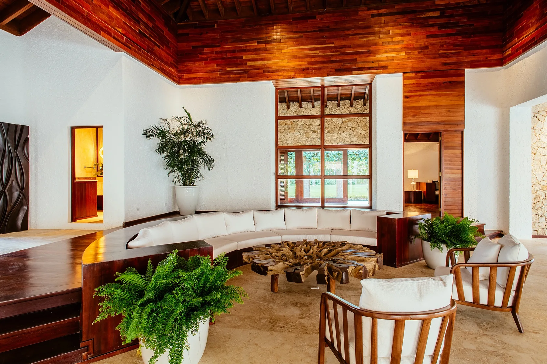 A spacious living room features curved seating beneath a high wooden ceiling.