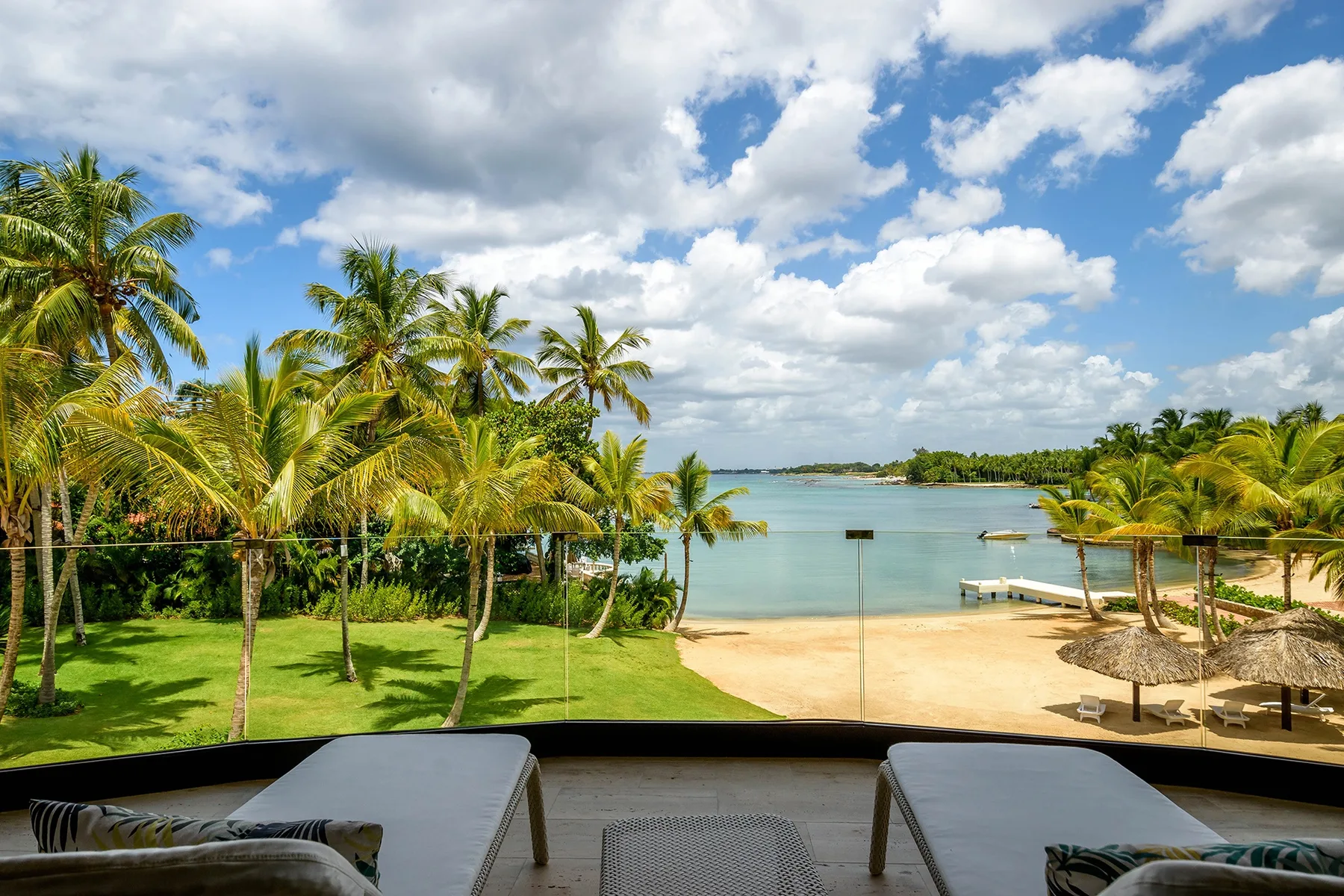 A tropical beach and calm water are visible beyond a palm-lined lawn and outdoor seating.
