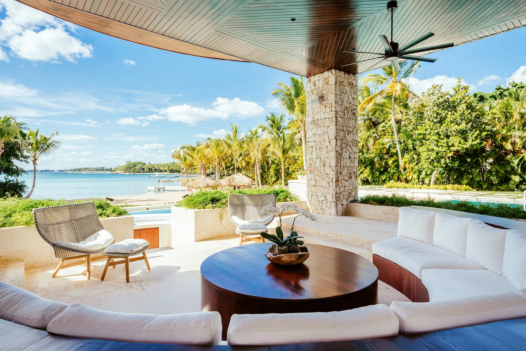 An open-air lounge overlooks a pool, with cushioned seating and tropical greenery.