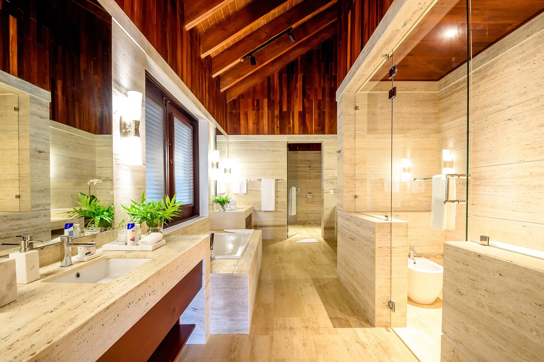 A spacious bathroom with pale stone counters, sinks, and a glass shower.
