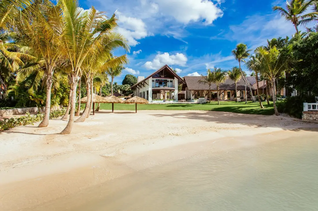 A palm-lined beachfront faces a large building across a sandy shore.