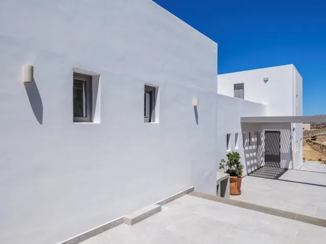 Exterior de edificio blanco con patio pavimentado y una zona de estar sombreada.