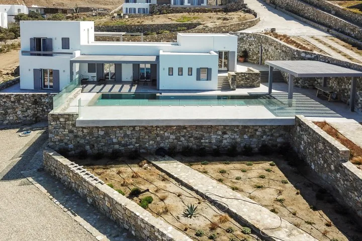A modern white house overlooks a rectangular pool and stone terraces.