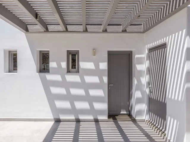Patio cubierto con una puerta gris y sombras a rayas sobre el suelo.