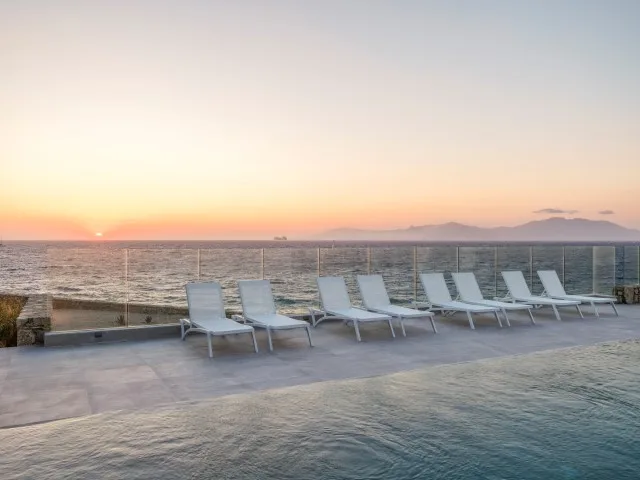 Una terraza junto al mar con asientos reclinables da al océano al atardecer.