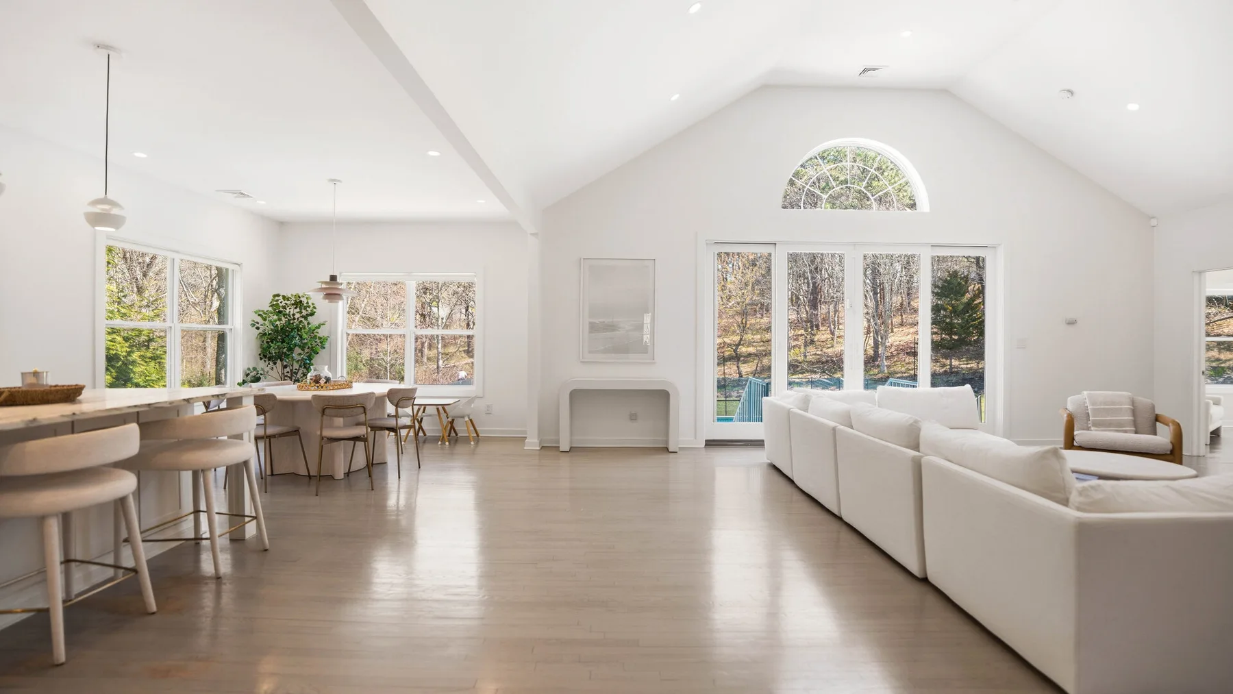 Una luminosa sala-comedor de espacio abierto con grandes ventanas y un sofá seccional blanco.