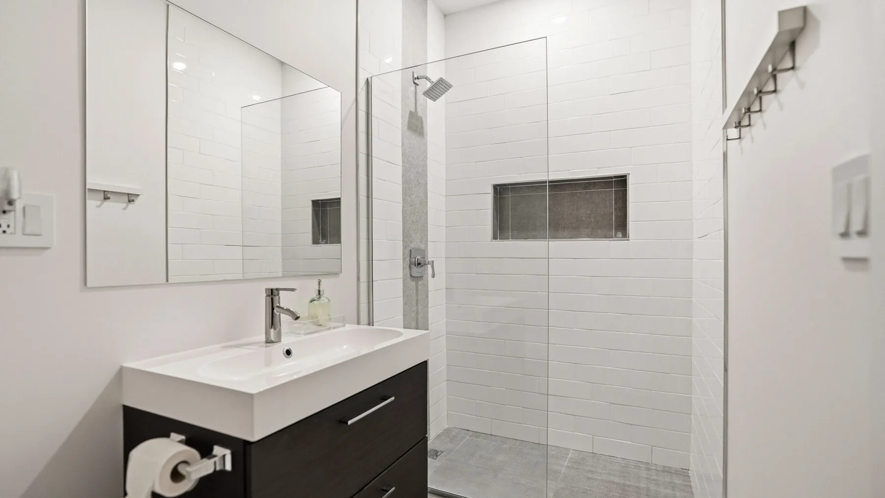 Un baño luminoso con un mueble oscuro y una ducha con mampara de vidrio.