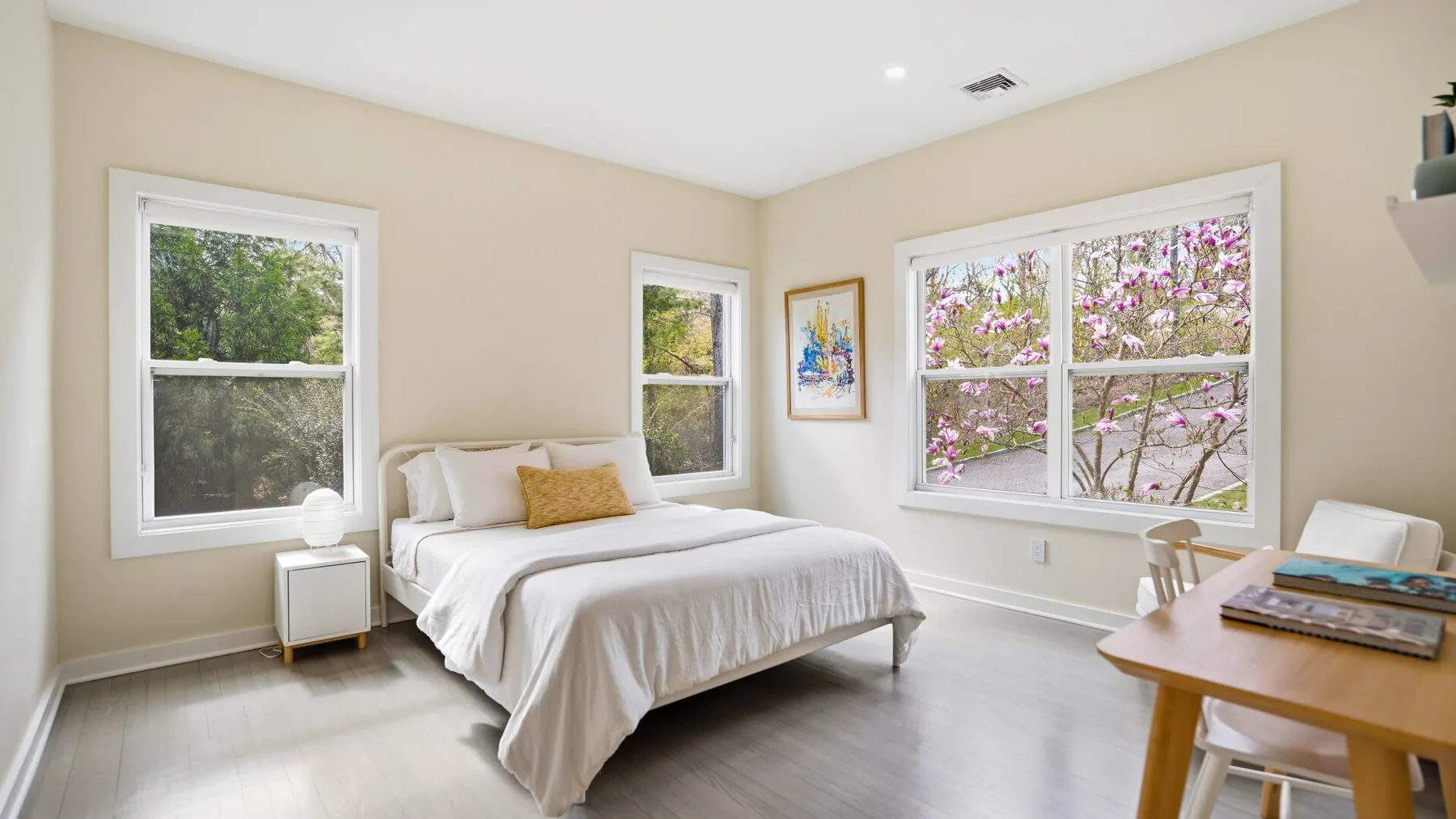 Un dormitorio luminoso con una cama y ventanas con vista a árboles en flor.