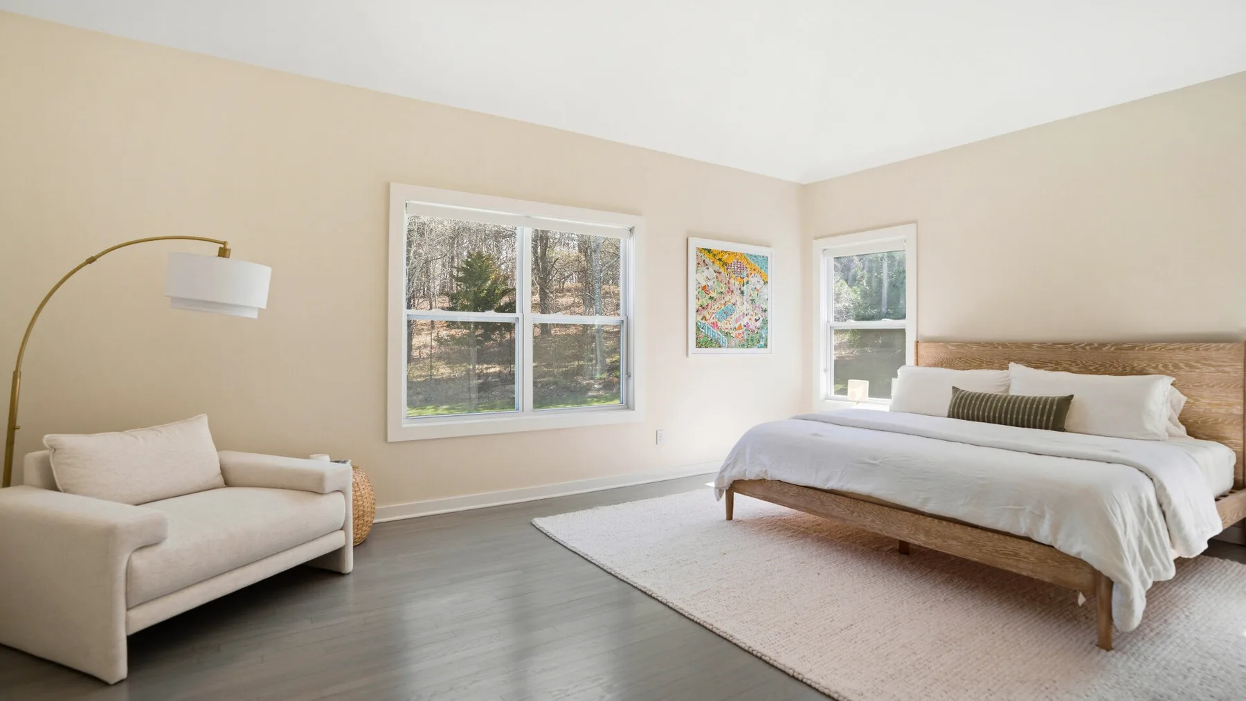 Un dormitorio luminoso con cama, zona de descanso y ventanas grandes.