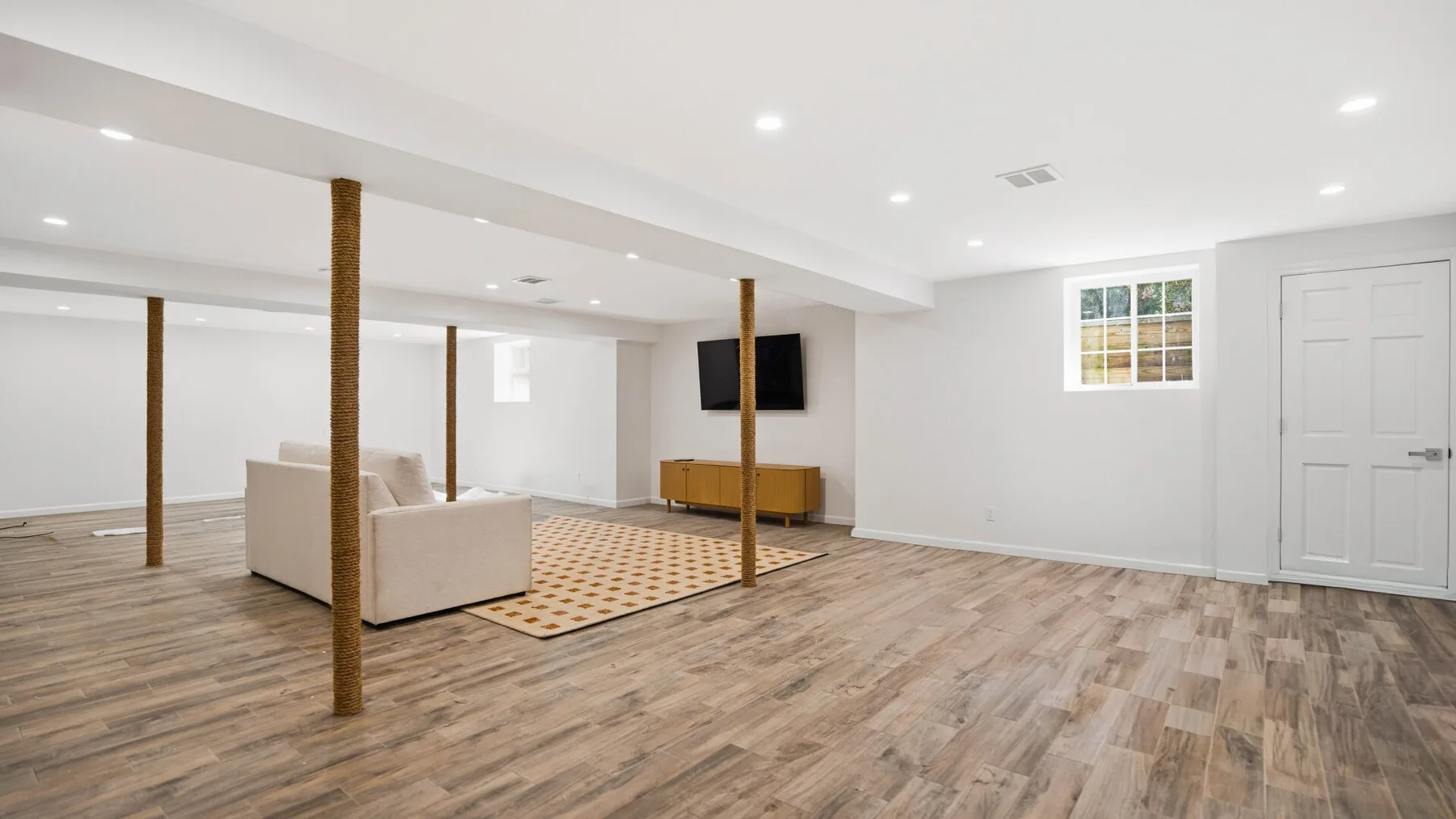 Una luminosa sala en un sótano con asientos, piso de madera y un televisor montado en la pared.