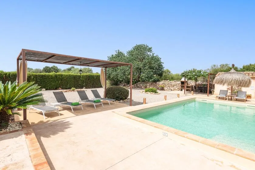 An outdoor swimming pool sits beside a shaded seating area and thatched umbrellas.