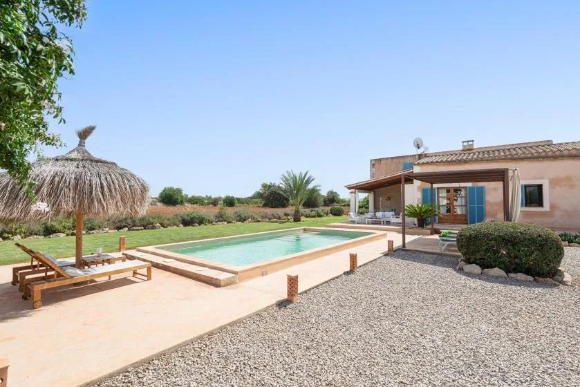 Outdoor swimming pool beside a house, with a shaded seating area and gravel patio.