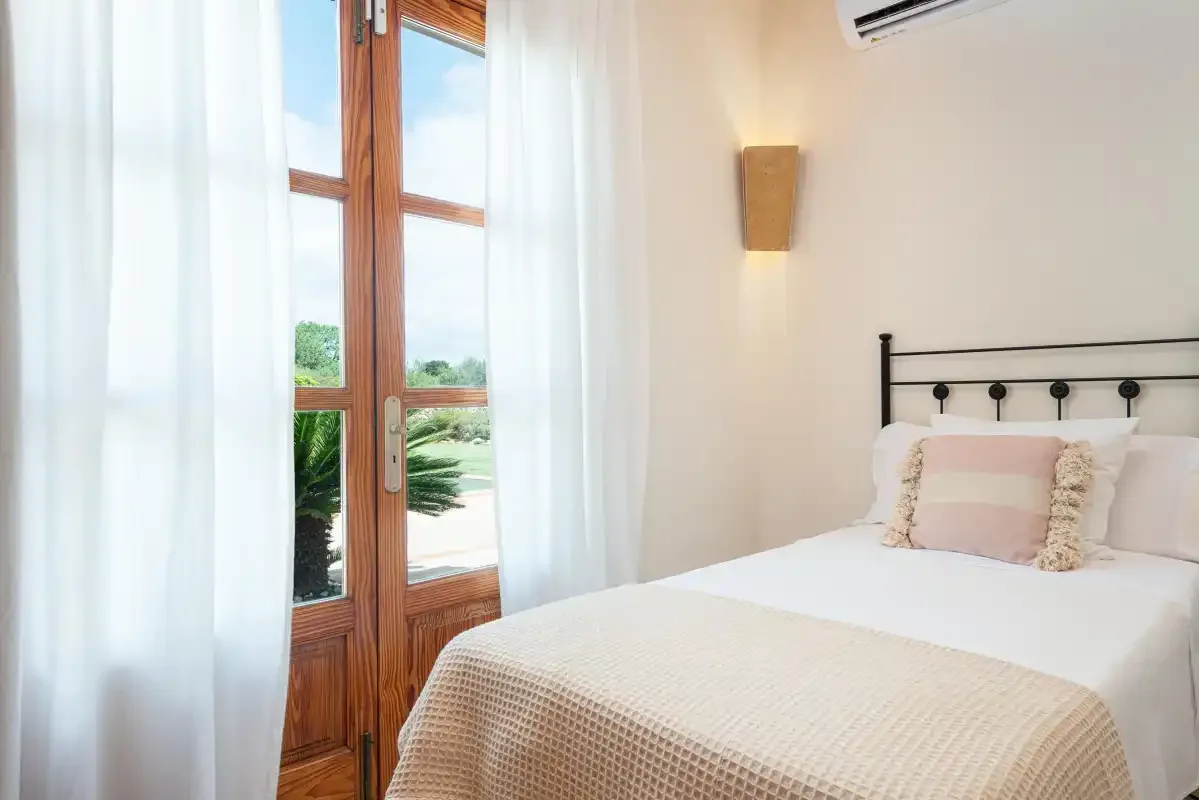 A bright bedroom with a bed beside tall windows and sheer curtains.