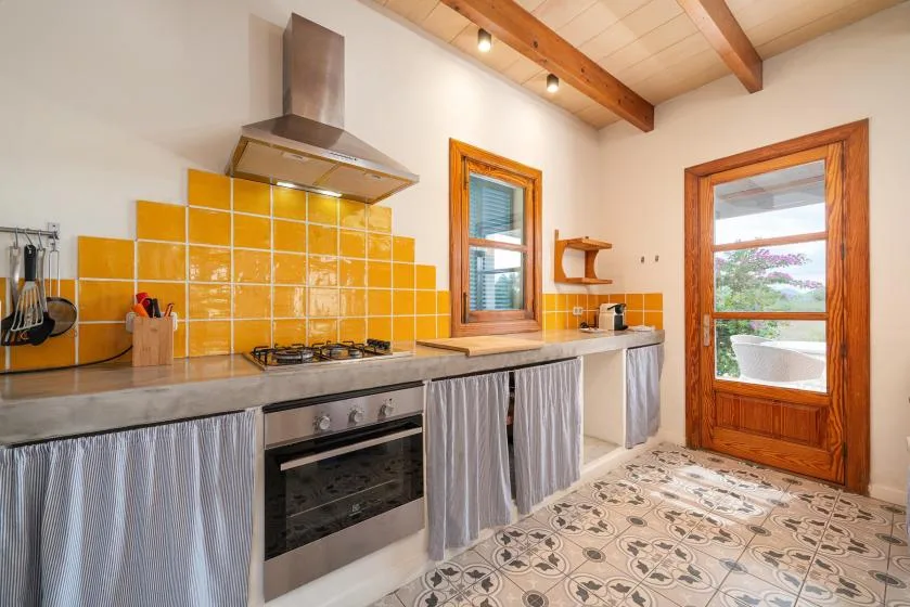 A kitchen with a cooktop, oven, and orange tile backsplash.
