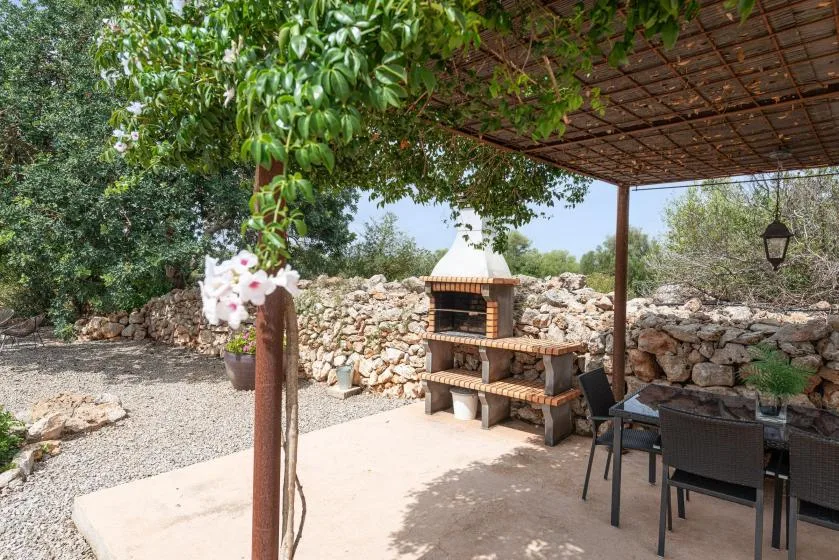 A shaded outdoor dining area beside a stone barbecue and garden.