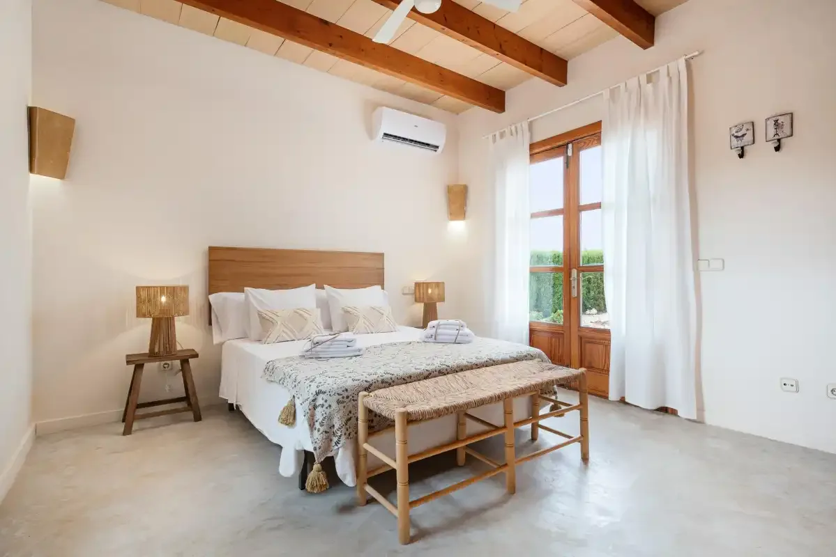 A bright bedroom with a bed, wooden ceiling beams, and a glass door.