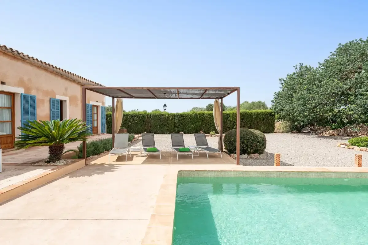 An outdoor pool beside a house, with shaded seating under a pergola.