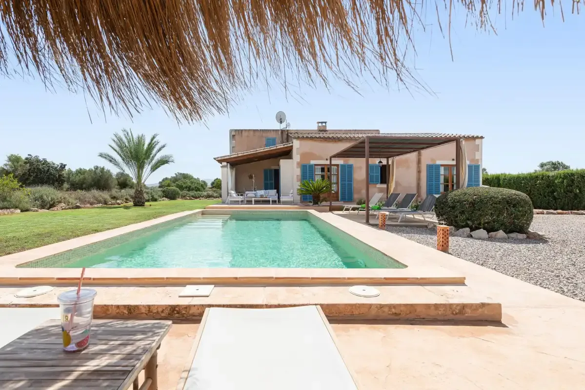 A swimming pool sits in front of a house, with lounge seating beside it.