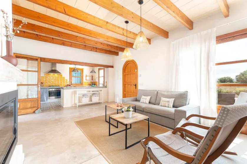 A bright living room with a gray sofa, armchairs, and an open kitchen.