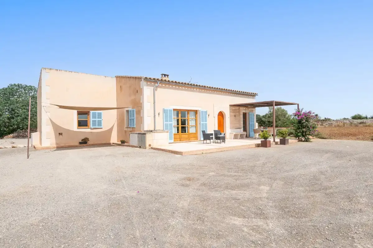 A single-story house stands beside a broad gravel courtyard under a clear sky.