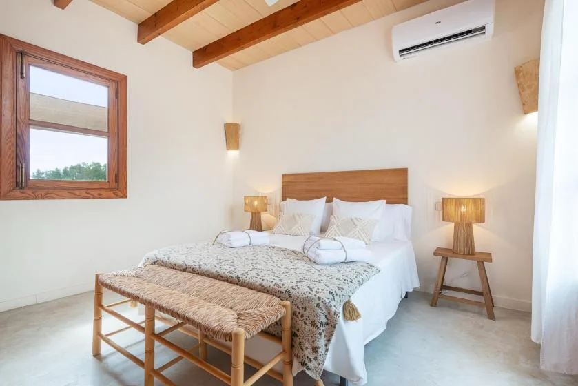A bright bedroom with a bed and a woven bench at its foot.